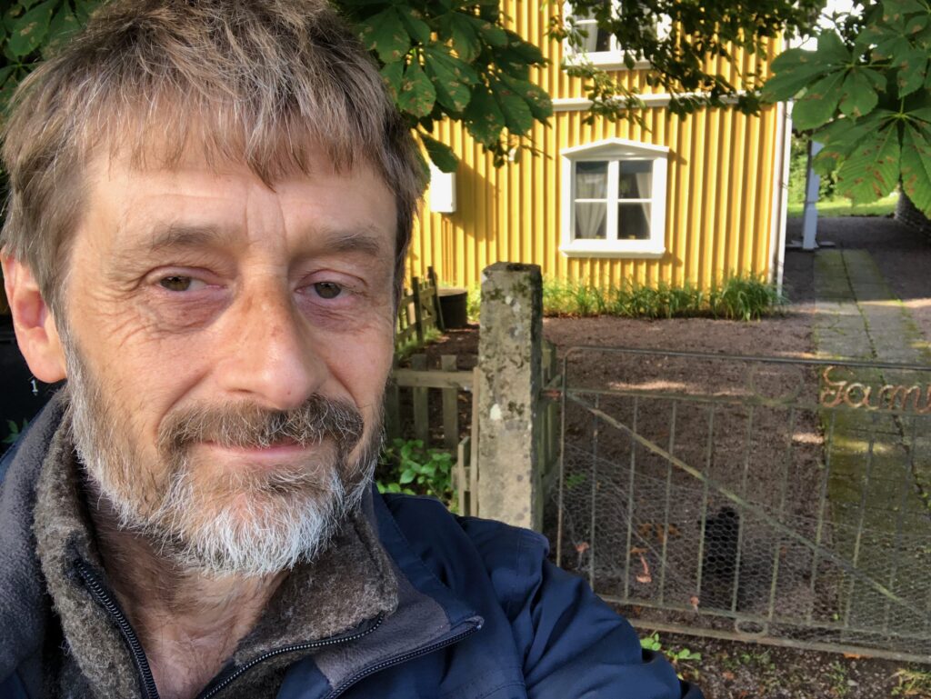 Seflieporträtt av Harald Bergengren. Utomhus med gul husgavel och grind i bakgrunden.